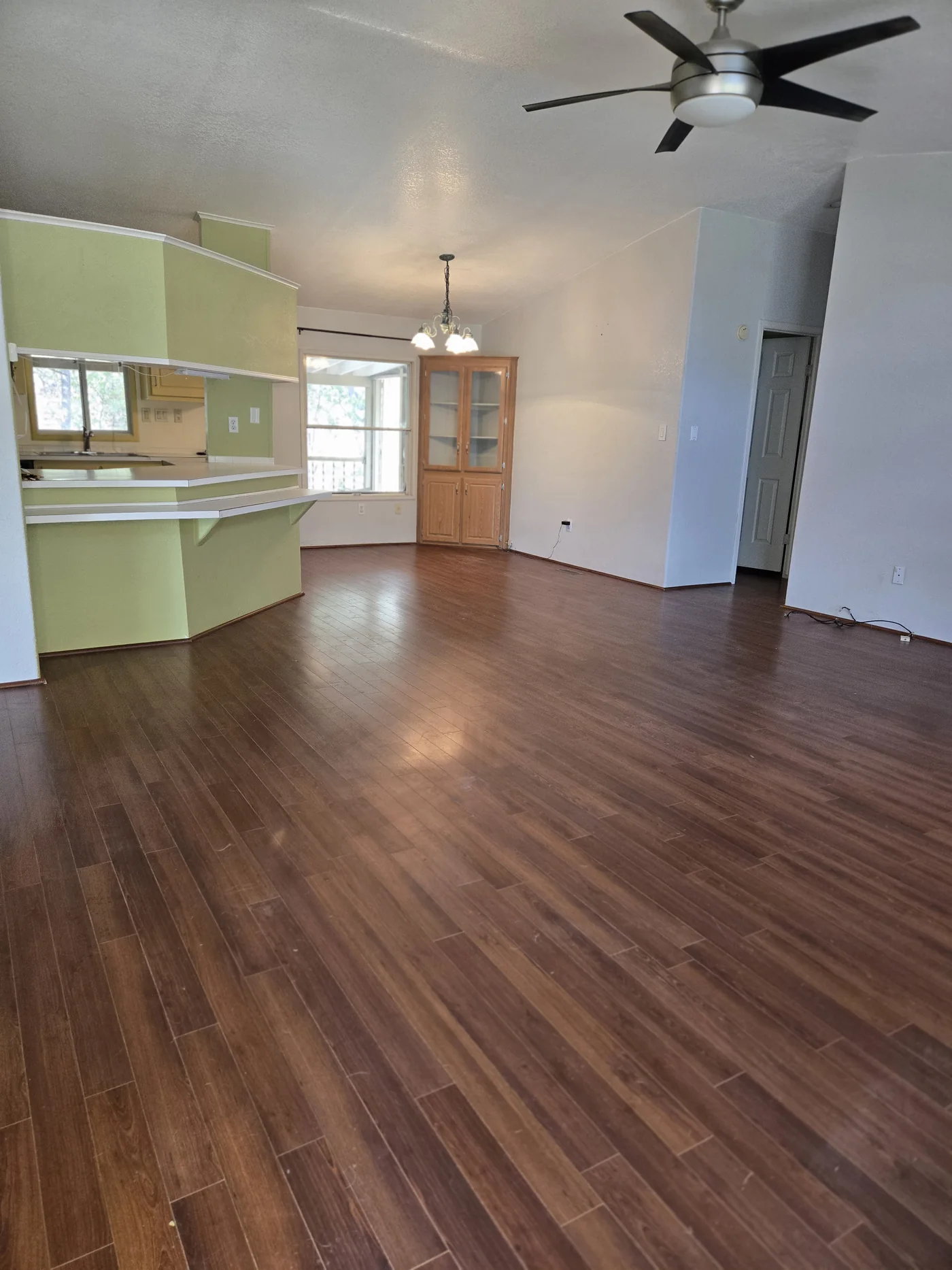 A cleared living area with wood flooring and an adjoining kitchen